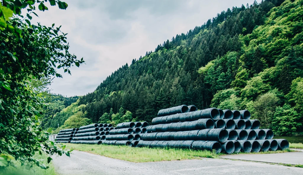 Gestapelte Stahlcoils im Freien vor bewaldeten Hügeln auf dem Außengelände eines Industriebetriebs
